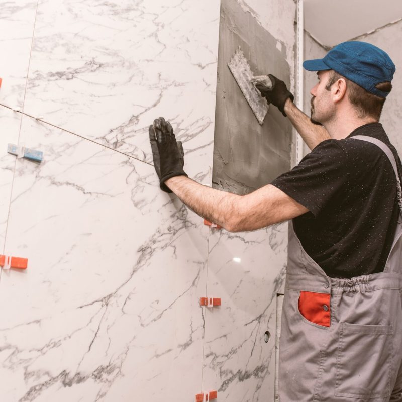 Handyman instaling ceramic tiles on the bathroom wall