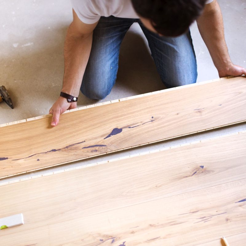 Unrecognizable handyman installing wooden floor in new house